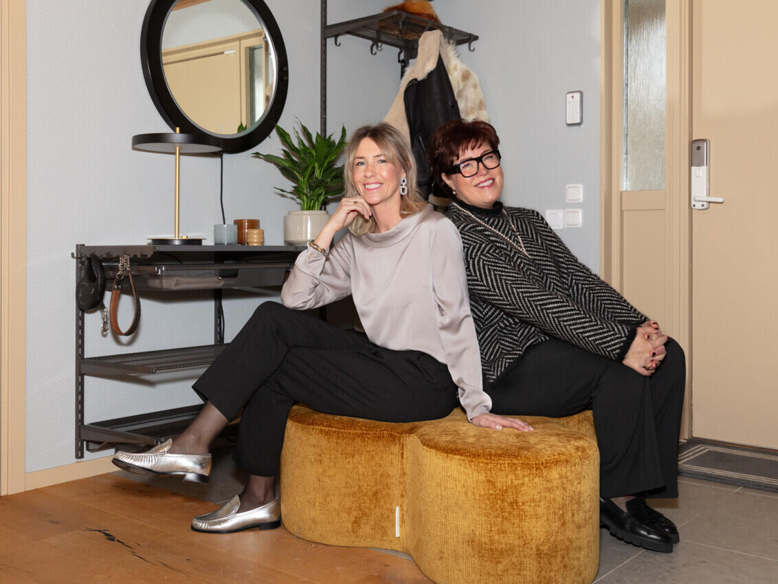 Christine Dalman og Jannicke Wistrand sitter på en puff i en gang med et åpent garderobeskap fra Elfa i grått.