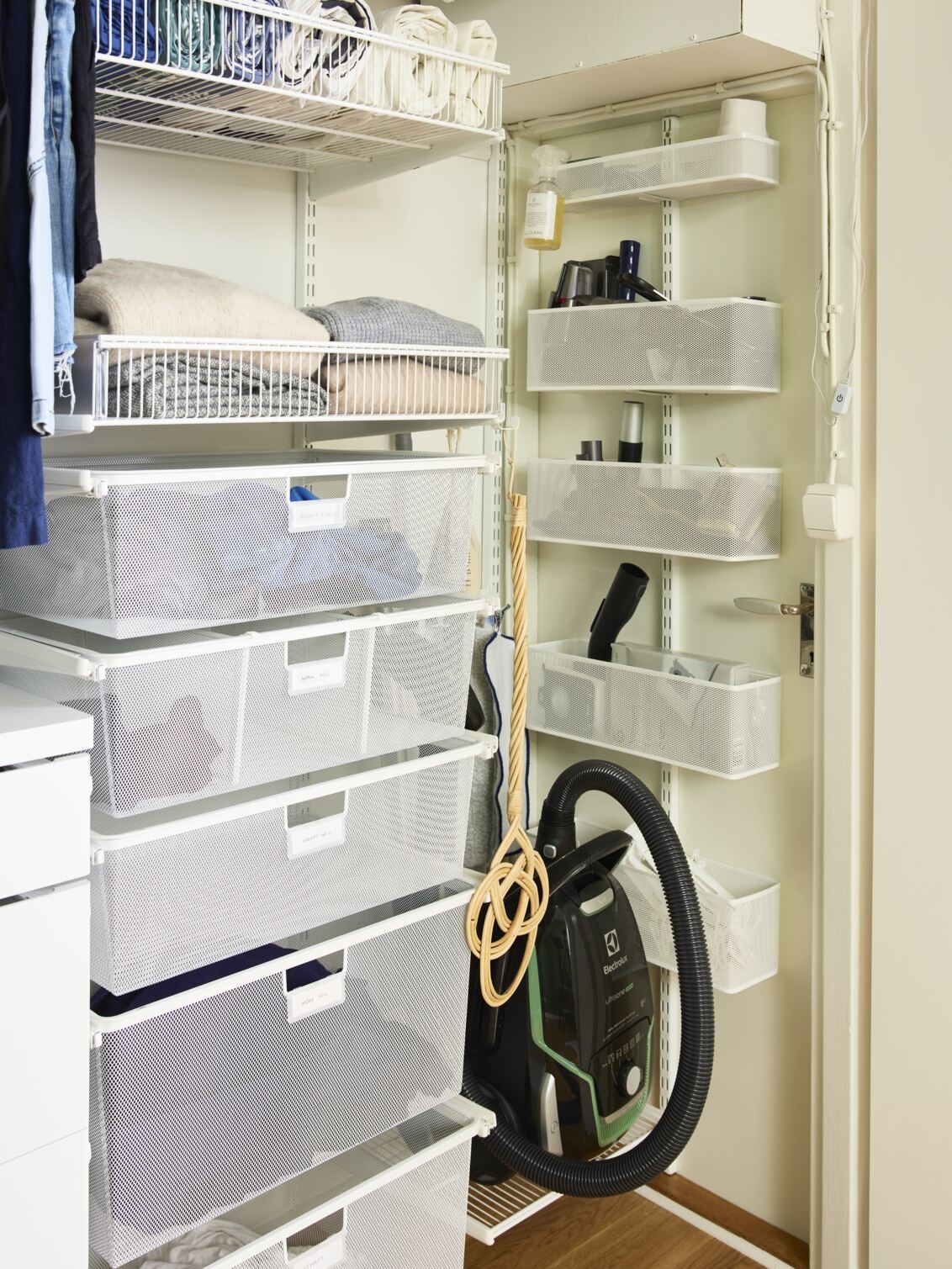 Kulma, jossa on Elfa-säilytyskalusteita, kuten lankakoreja, verkkokoreja ja verkkokoreja vaatteille ja siivoustarvikkeille.