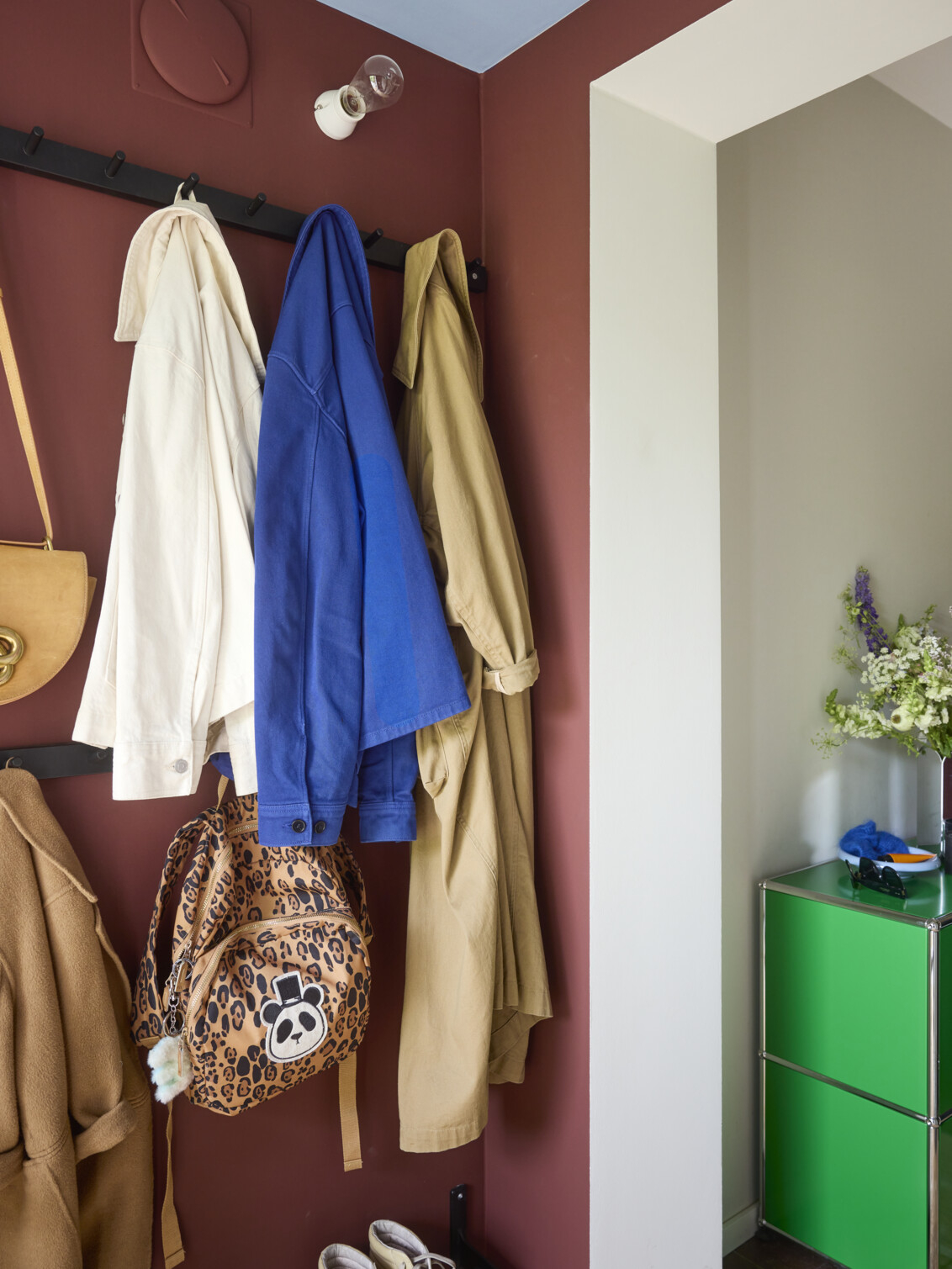 Hallway with burgundy walls and hooks where outerwear and bags hang.