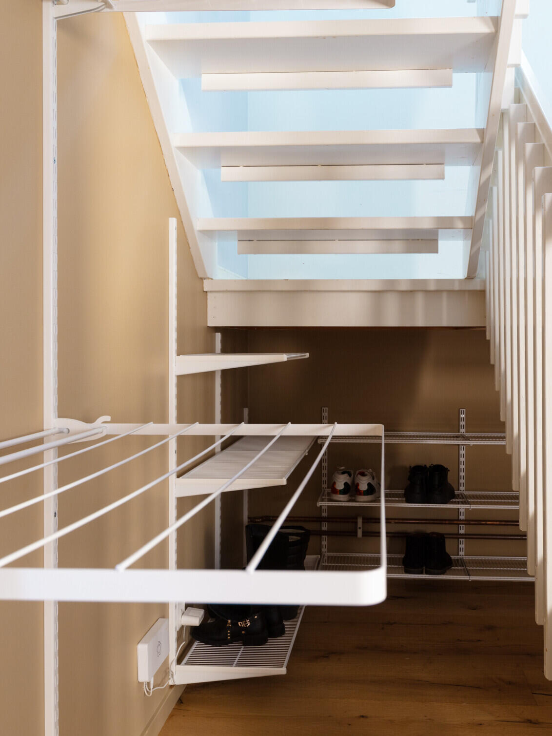 Området under trappen der det henger tørkehyller og trådhyller fra Elfa med sko oppå.