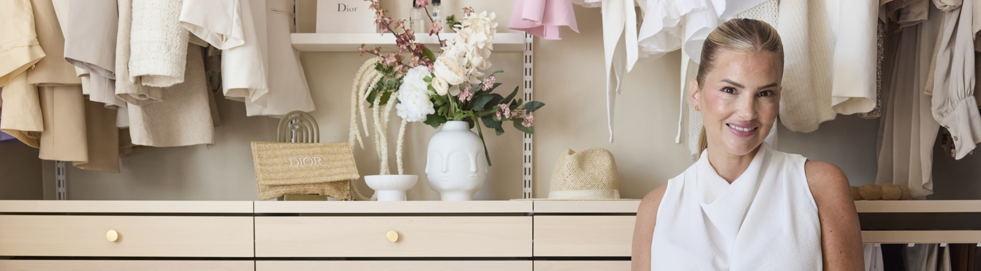 Ida-Marie is sitting by an open wardrobe from Décor+ by Elfa in white and birch.