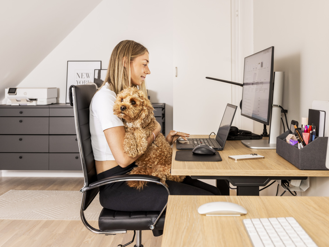 Lisa Lilja is sitting with her dog at the computer in a home office with a sideboard from Décor+ by Elfa with grey drawer boxes.