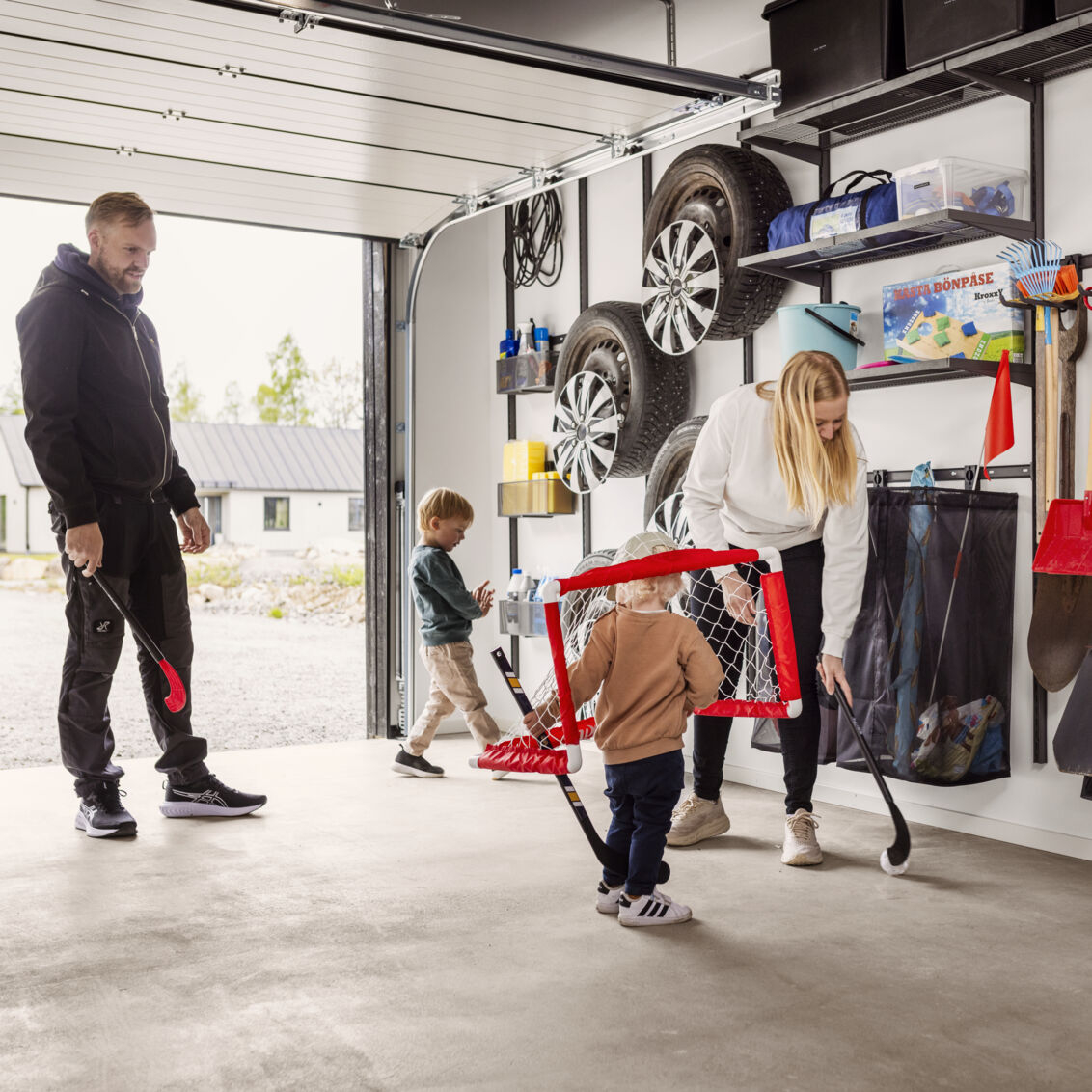 A family with young children playing bandy in a garage with Garage+ by Elfa storage.