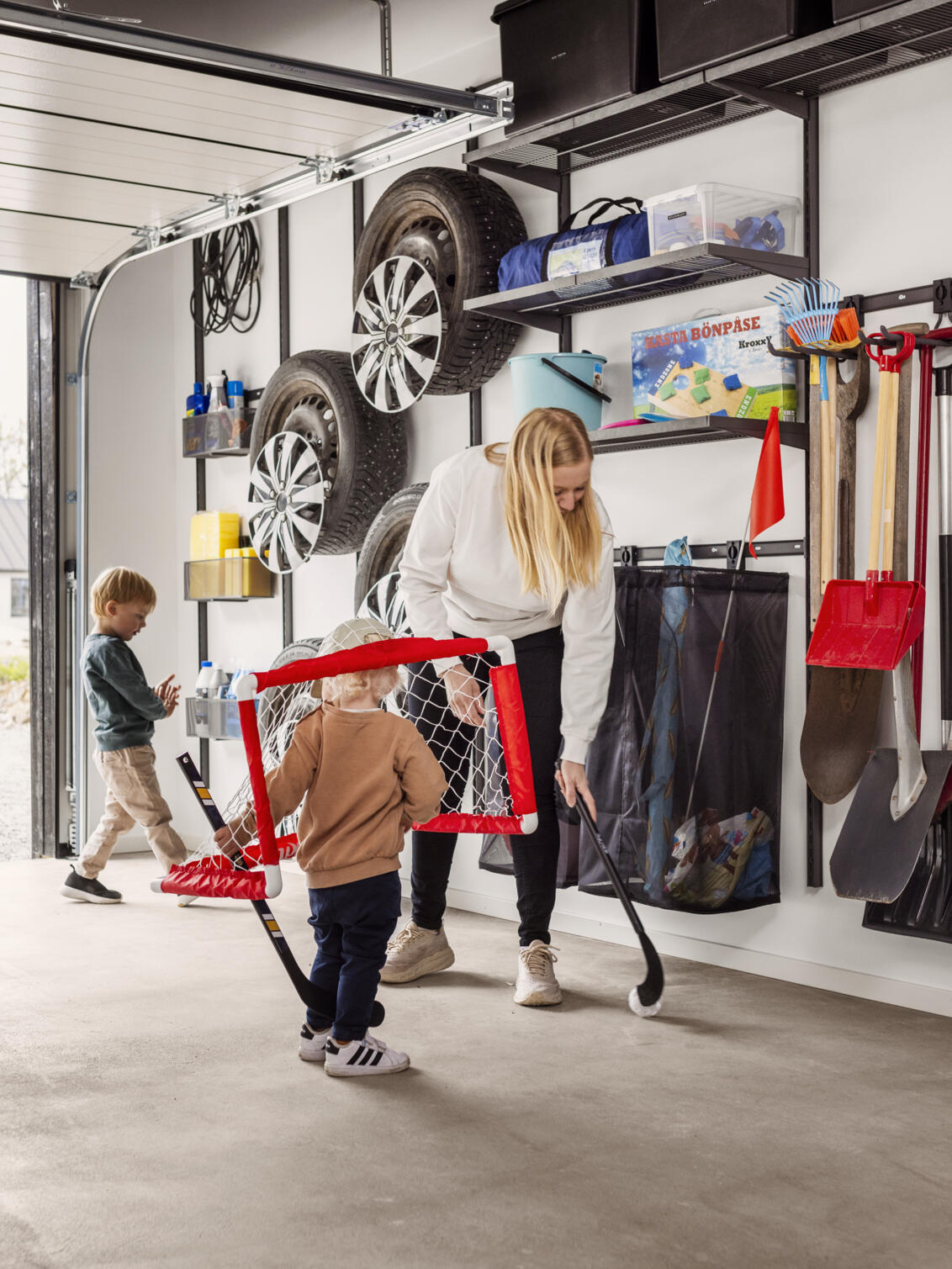 A family with young children plays bandy in a garage with Garage+ by Elfa storage.