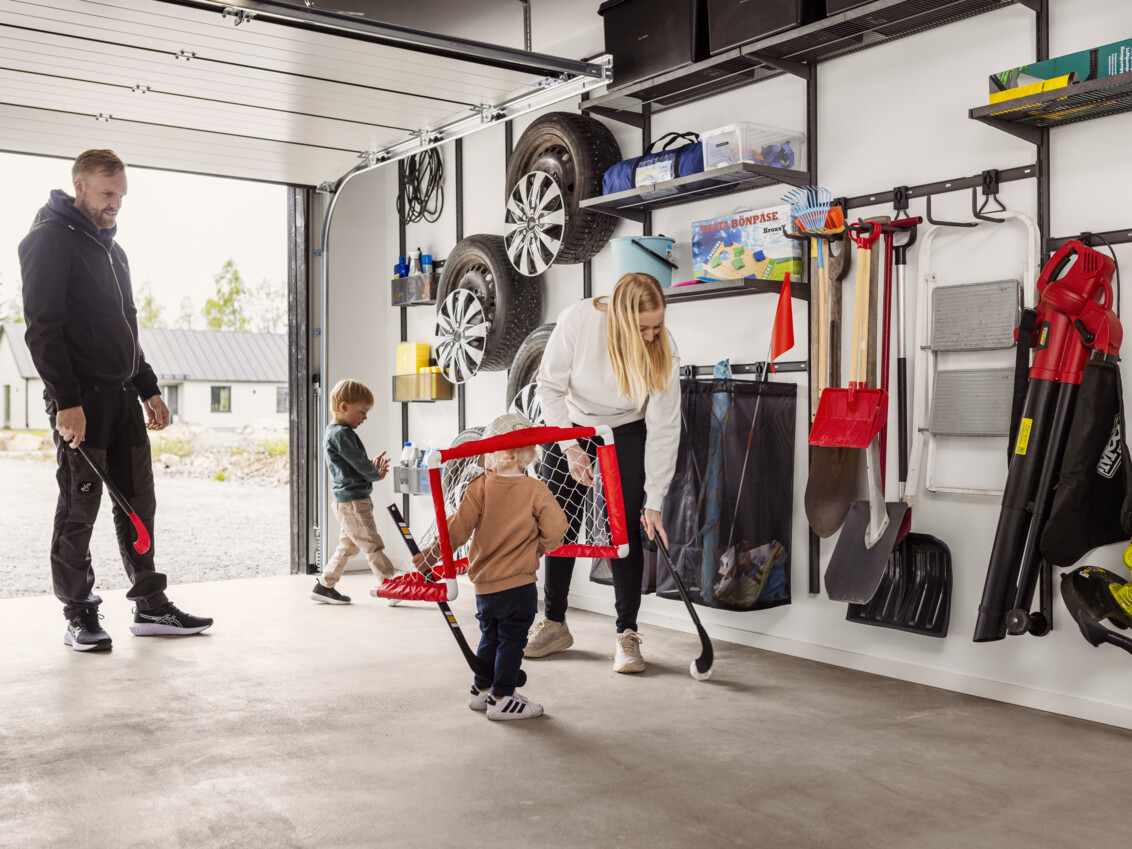 A family with young children playing bandy in a garage with Garage+ by Elfa storage.