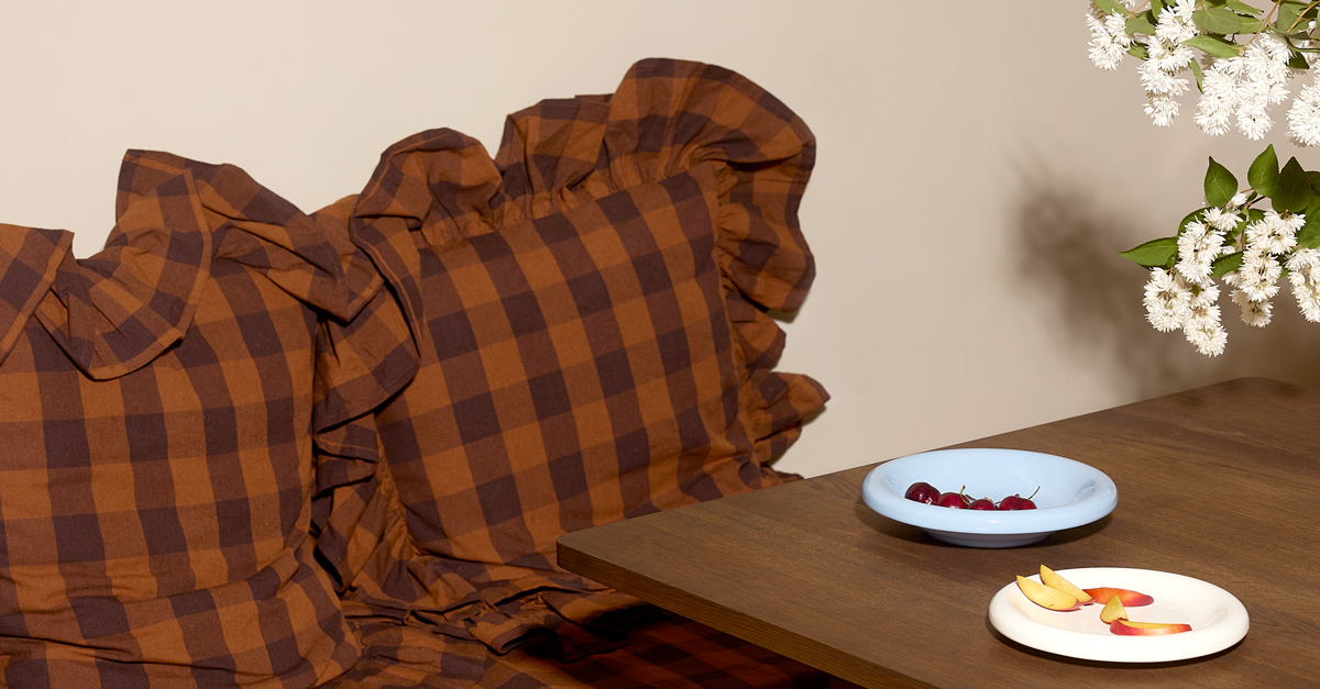 Checked pillows in brown at a table with small plates with fruit and berries.