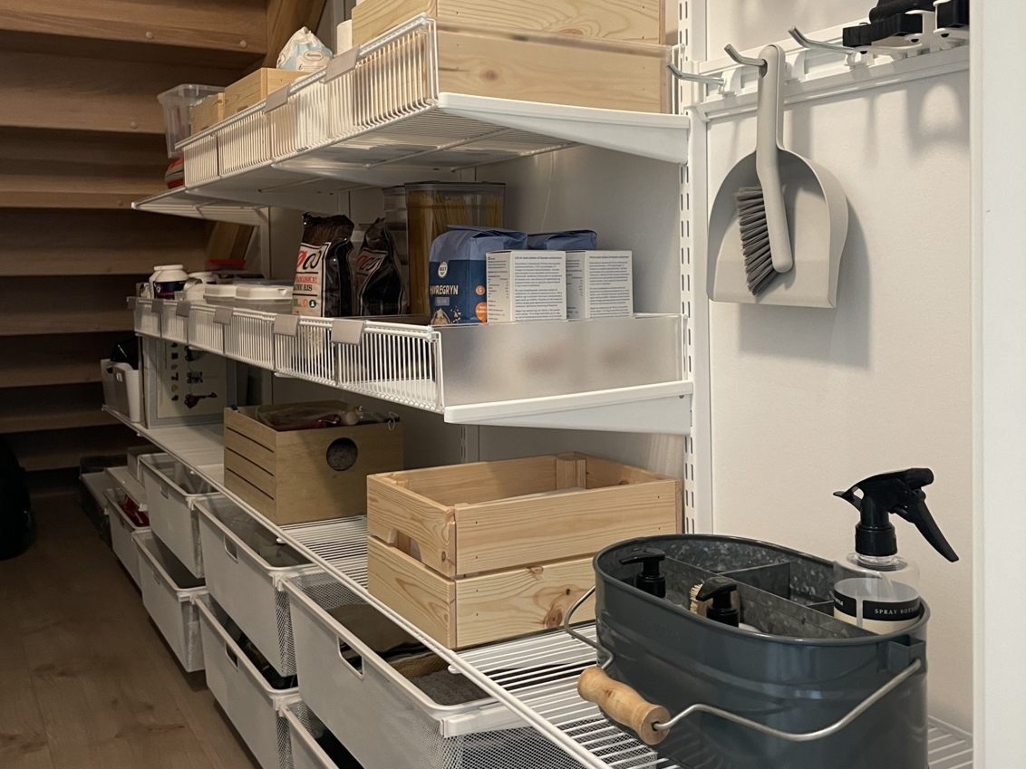 Classic by Elfa -säilytyskalusteita sisältävä kaappi portaiden alla, joka sisältää kuiva-aineita ja siivoustuotteita.