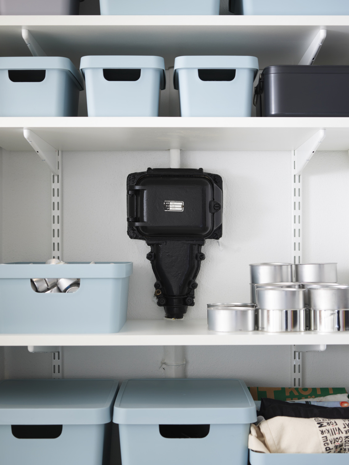 Valkoinen Sparring by Elfa -hylly, jossa on siniset säilytyslaatikot sähkökaapin ympärillä.