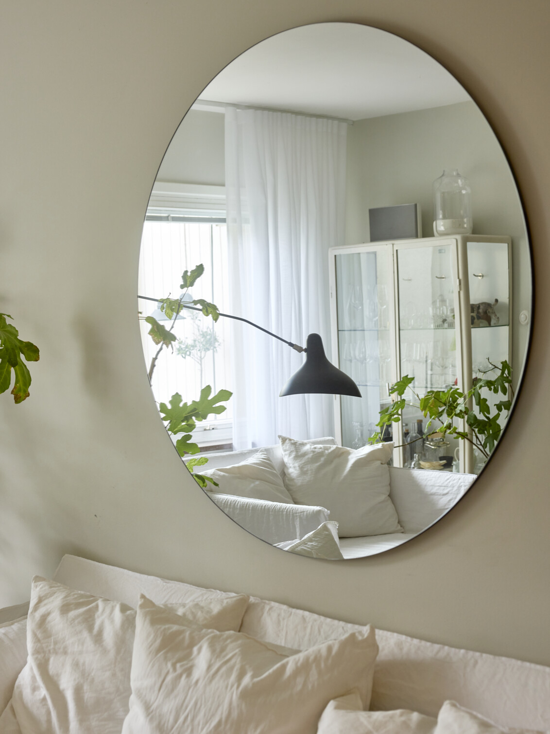 A mirror above a sofa where a window and a glass cabinet can be seen in the mirror image.