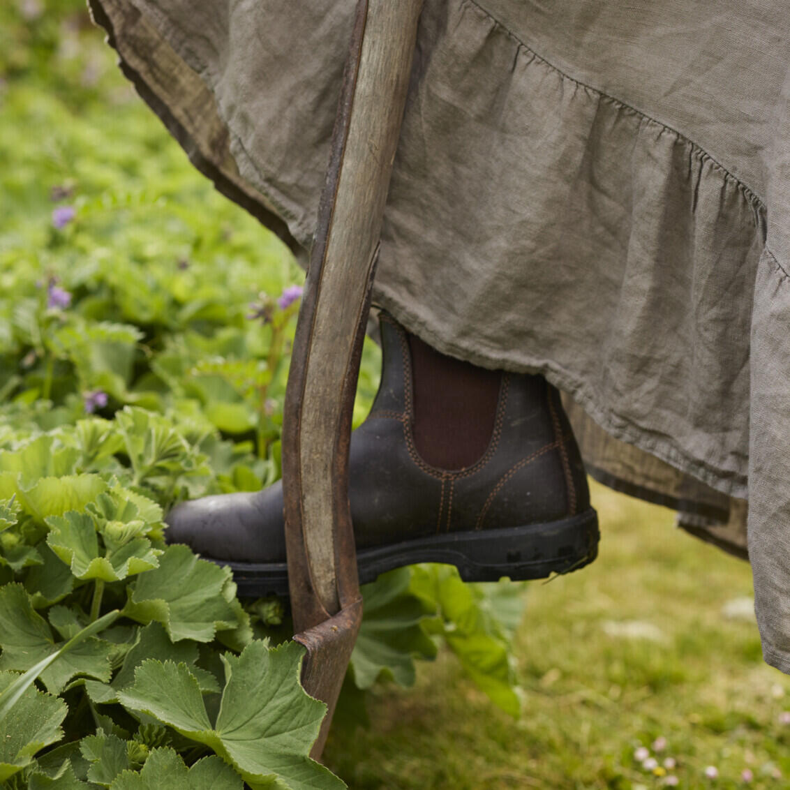 Carin has her foot on a shovel in the garden.