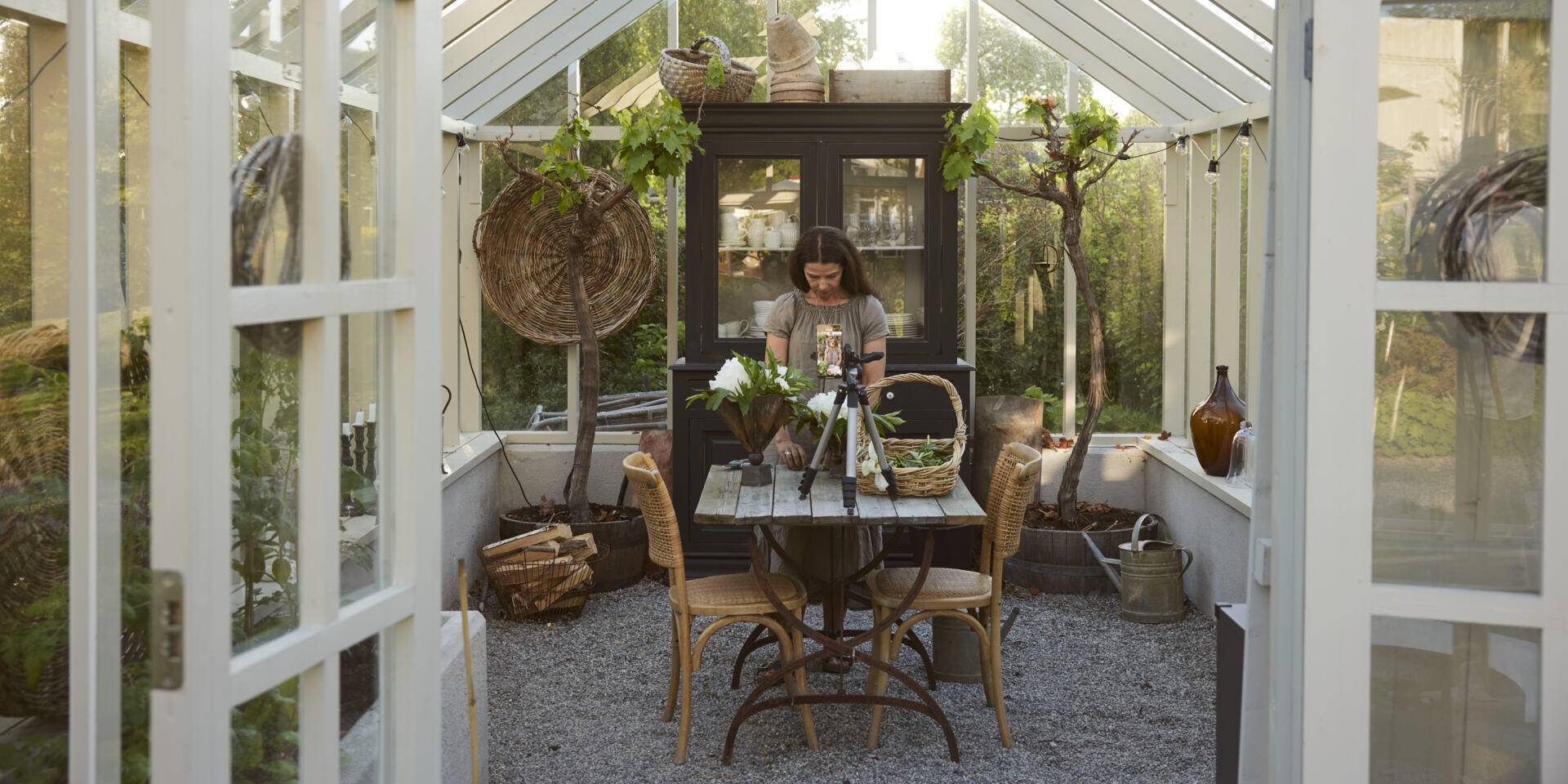 Carin takes a picture with her mobile while she arranges flowers on the garden table in her greenhouse.