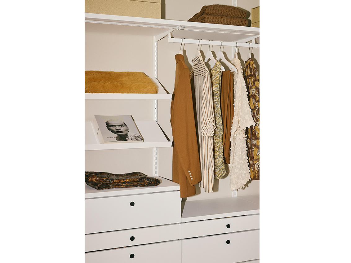 Hanging clothing in a Décor+ by Elfa wardrobe in white with pull-out drawers.