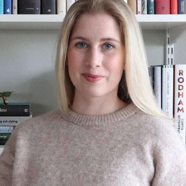 A woman stands in front of a shelving system with books