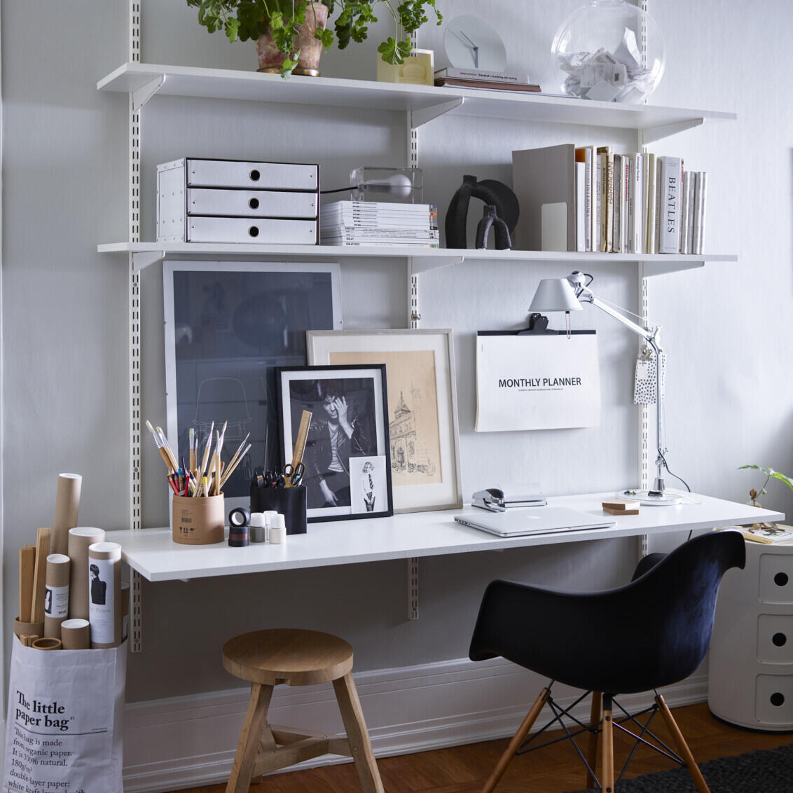 A home office with Elfa’s classic wall-mounted "Sparring" shelving system, a black office chair and a wooden stool.