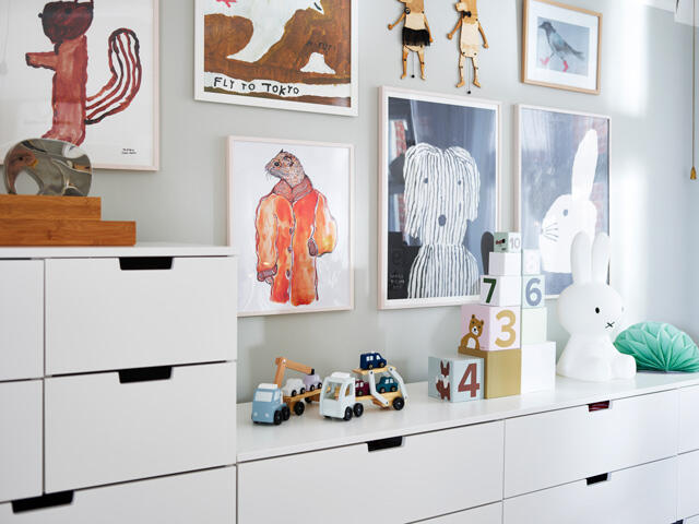Białe pudełka Elfa z czarnymi uchwytami w pokojach dziecięcych z kolorowymi obrazami i zabawkami