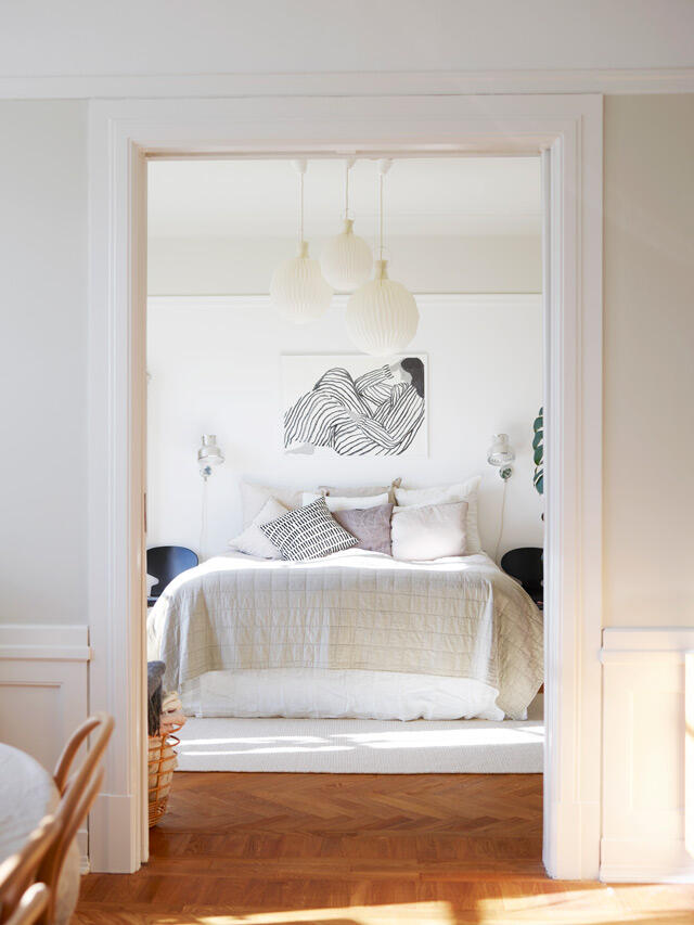 Jasna sypialnia z białymi ścianami, drewnianymi podłogami i wiszącymi lampami w stylu skandynawskim