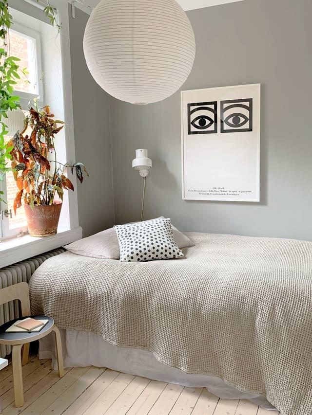 Sypialnia z miętowo-zielonymi ścianami, okrągłą lampą sufitową i rośliną doniczkową przy oknie