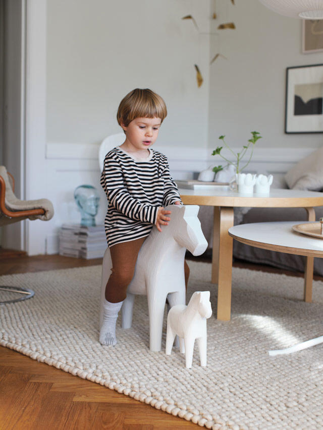 Dzieci Alvar bawią się białym zabawkowym koniem w jasnym salonie z drewnianą podłogą i naturalnym światłem