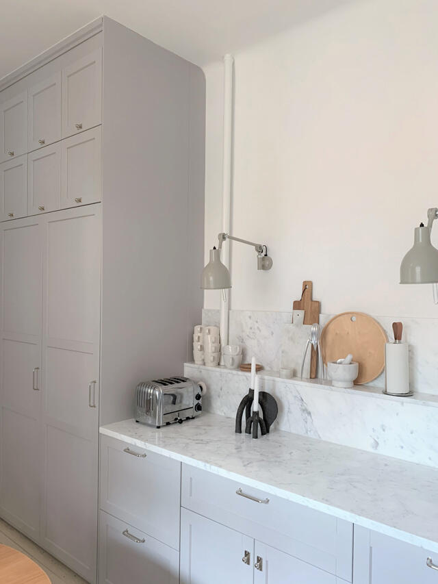 Jasna kuchnia przed rozwiązaniem Elfa z białymi szafkami, marmurowym blatem i drewnianymi deskami do krojenia