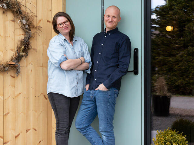 Couple of mountain castle family in front of modern house entrance with wood paneling and glass door