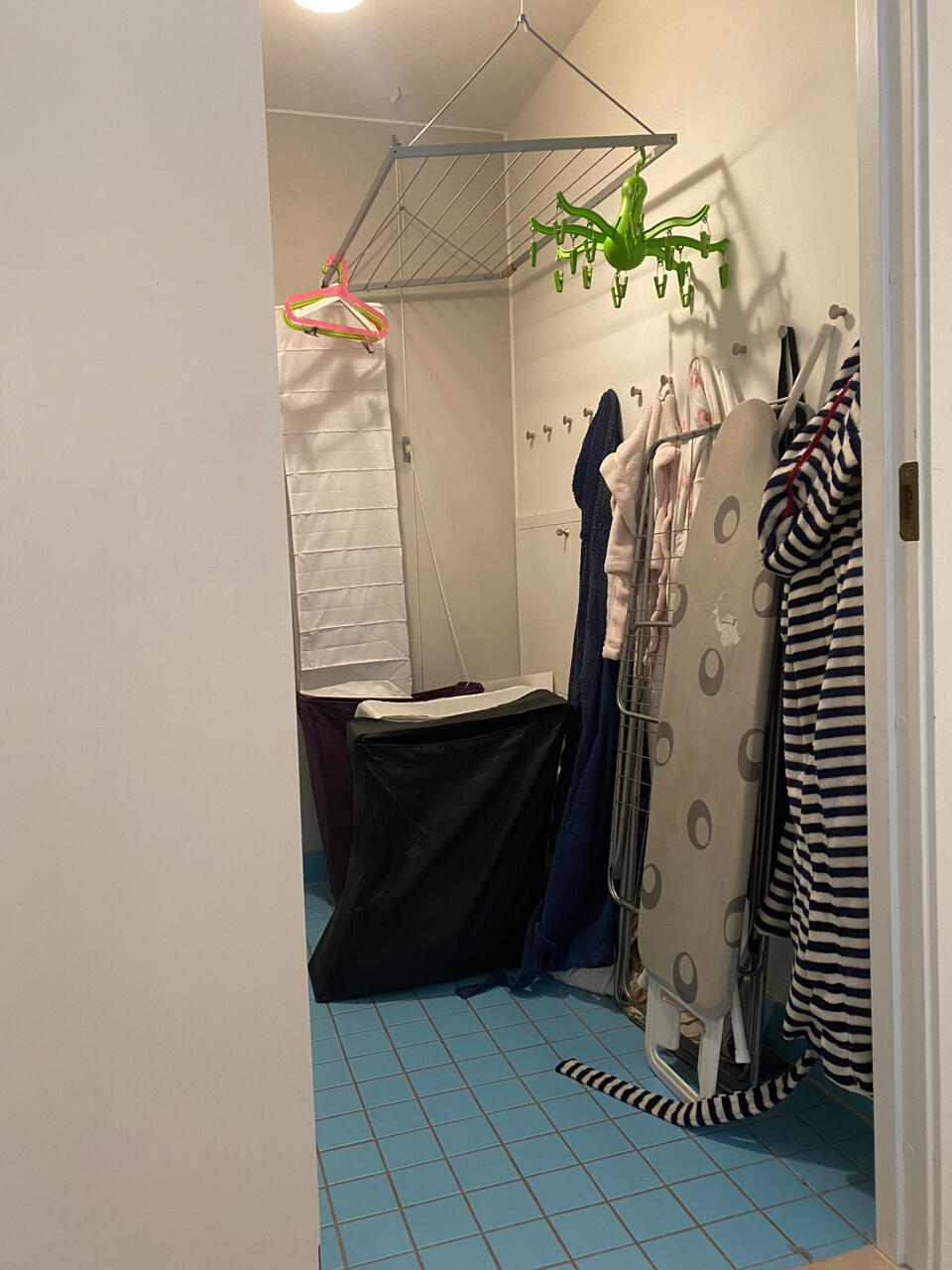 Niki Barntmark Área de servicios desorganizada con artículos de lavandería y tabla de planchar, requiere un sistema de almacenamiento