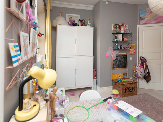 Dětský pokoj Haga s bílou skříní, šedými stěnami a barevnými hračkami, připravený na organizaci