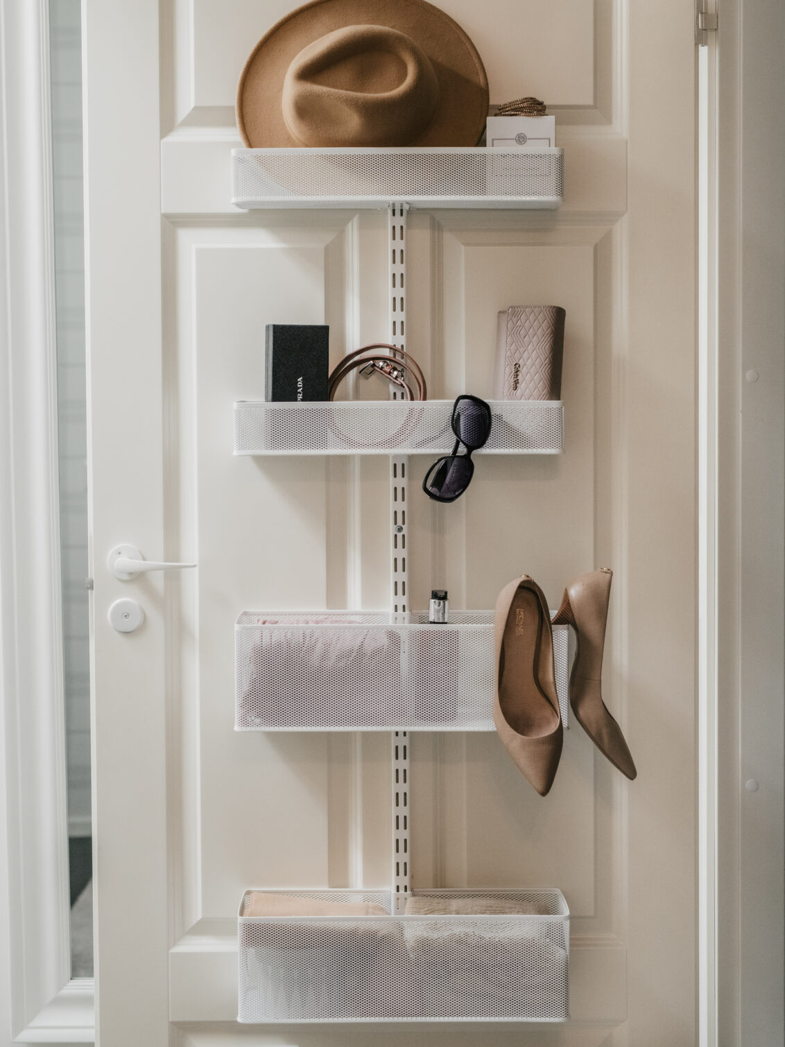 Valkoinen ovi ja Classic by Elfa -ovisäilytyskaluste, jossa on verkkokoreja, asusteita ja korkokenkiä.