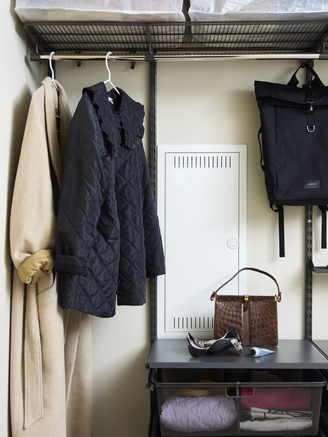 Harmaa Classic by Elfa -vaatekaappi, jossa on ulkovaatteita ja laukkuja, joiden säilytystila on rakennettu sähkökaapin ympärille.