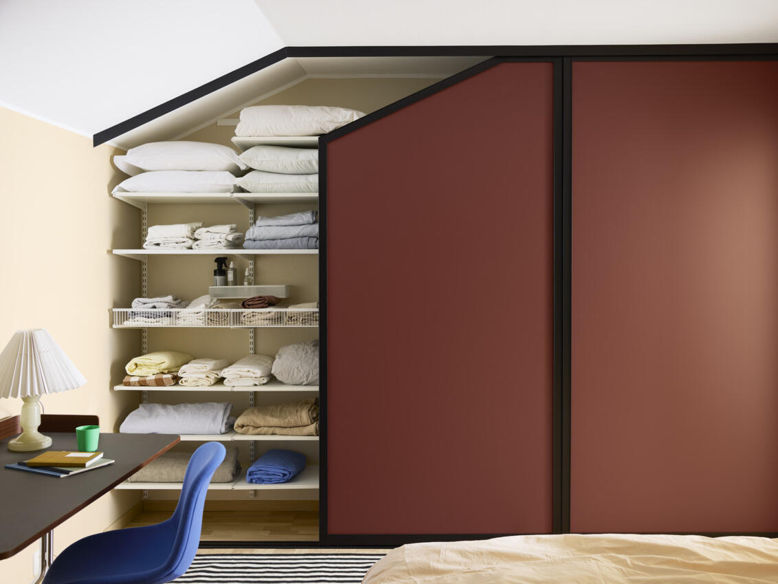 Schlafzimmer mit Kleiderschrank mit burgunderroten Schiebetüren von Elfa unter Dachschrägen.