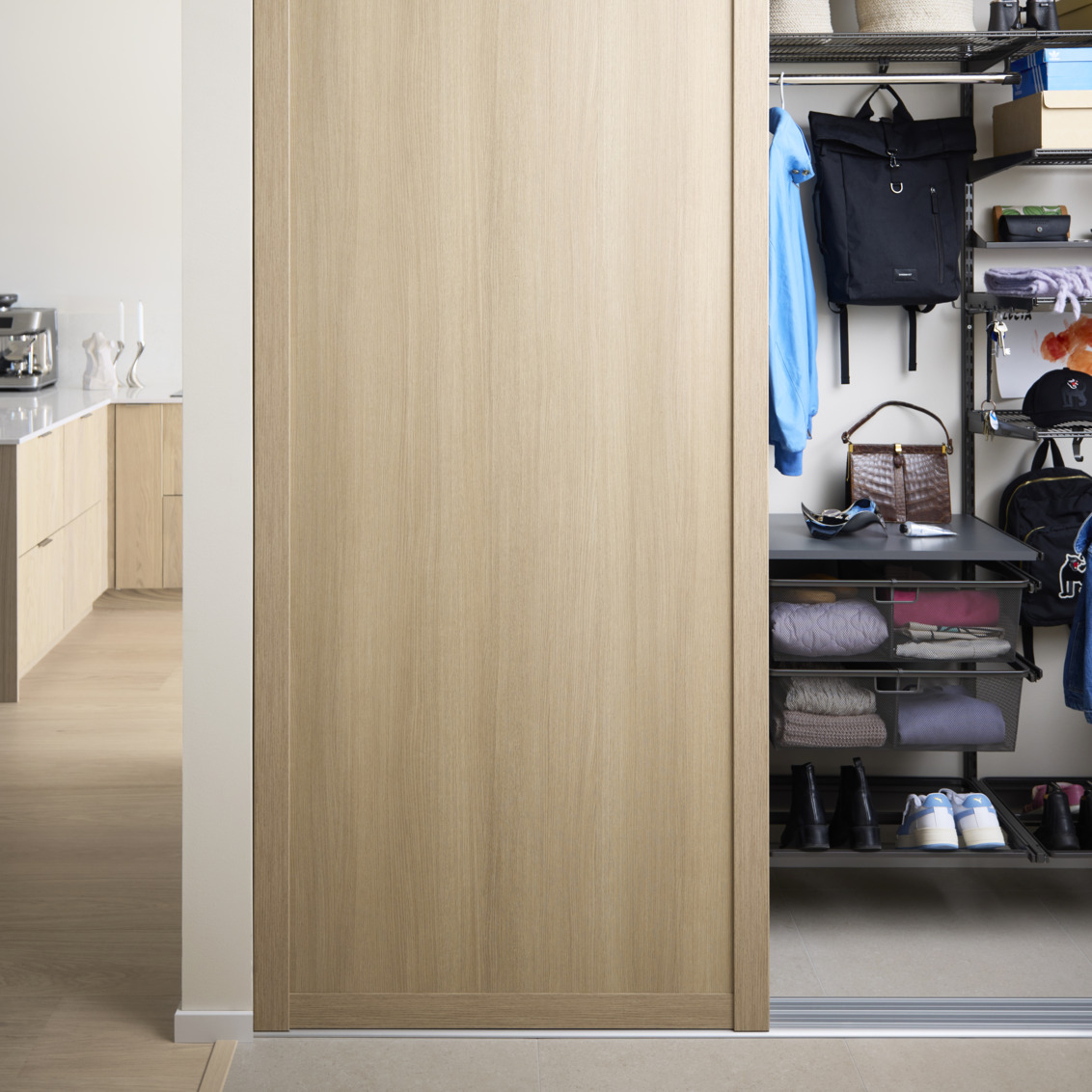 Eteinen, jossa on Elfa-vaatekaappi ja Grace-liukuovet, joiden täyte on vaaleaa tammea.