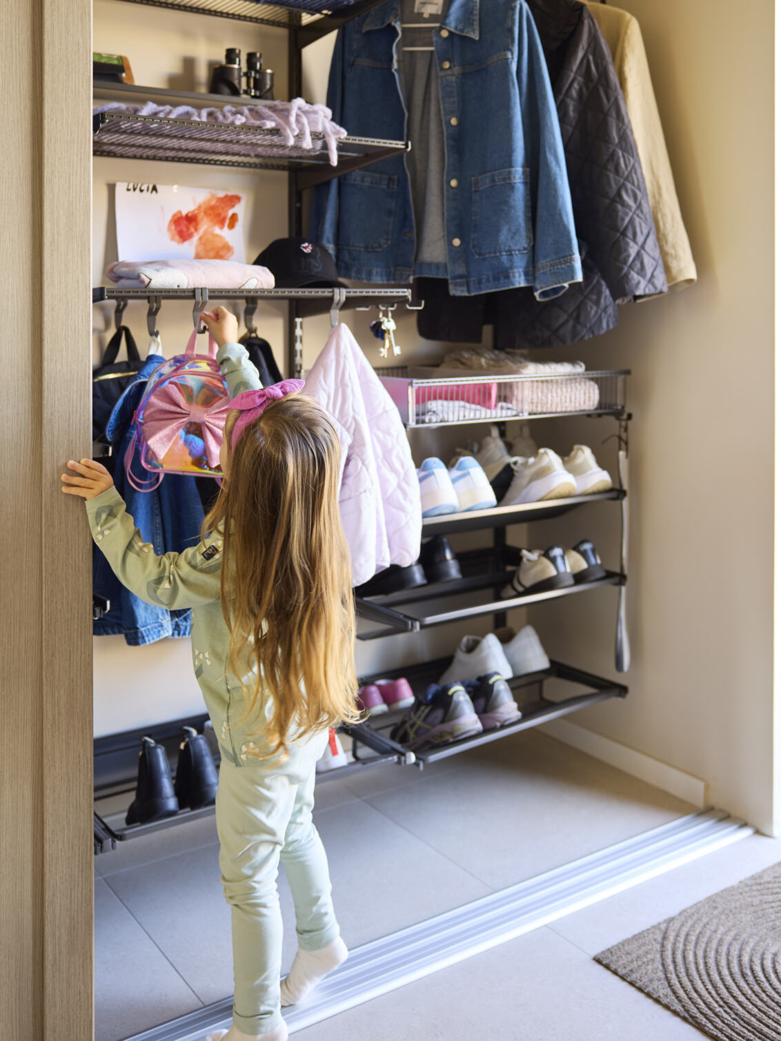 Eteinen, jossa on Classic by Elfa -vaatekaappi ja pieni tyttö ripustamassa reppua.