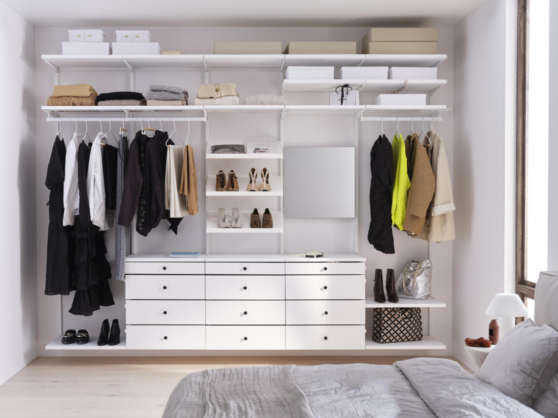 Schlafzimmer mit offenem Décor+ Kleiderschrank von Elfa mit hängender Kleidung, schrägen Regalen, Spiegel und Schubladen in weiß.