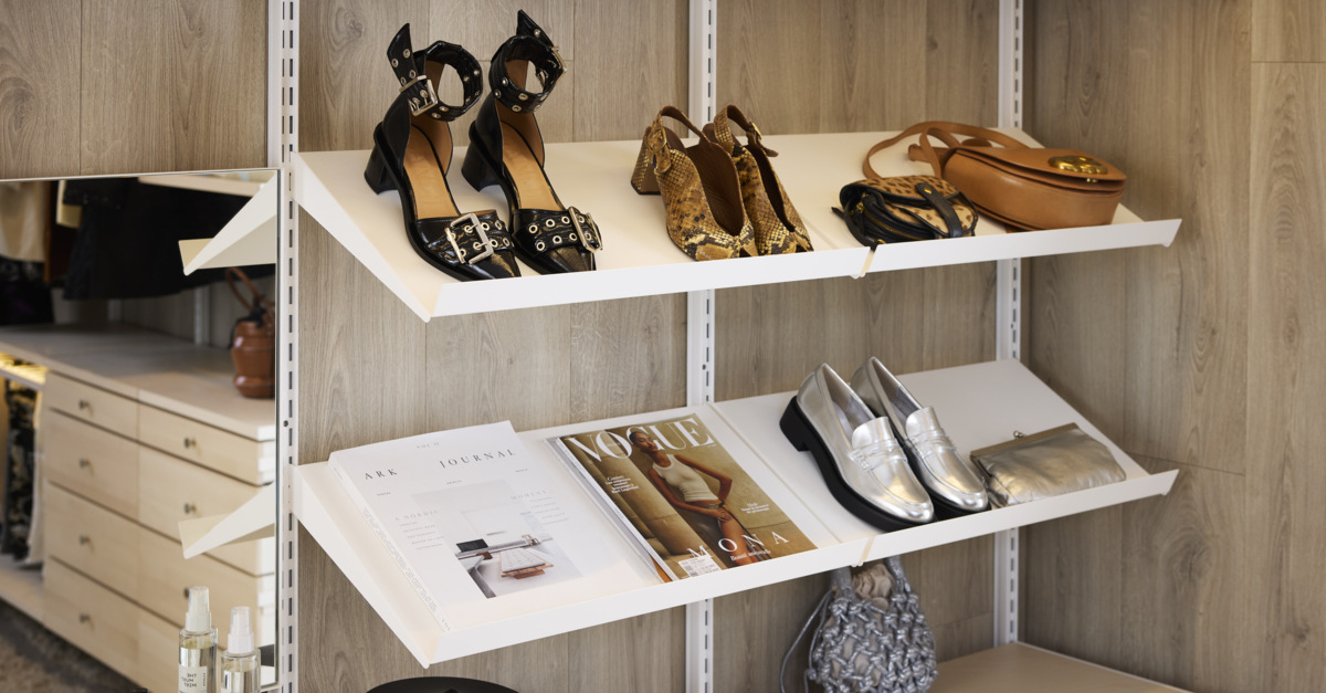 En Décor+ by Elfa-garderobe i hvitt og bjerk med vinklede hyller som inneholder sko og vesker.