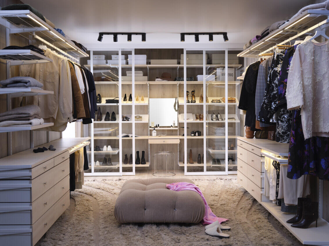 Luksuriøst walk-in closet med beige, puff og Décor+ oppbevaring fra Elfa, som har arktiske skyvedører i glass.