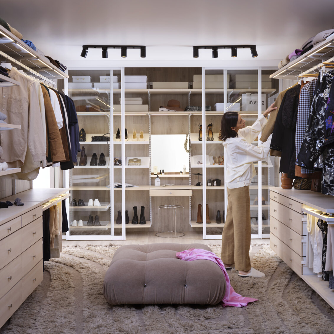 A woman is looking for clothes in a walk-in closet with Décor+ clothes storage from Elfa in white and birch.