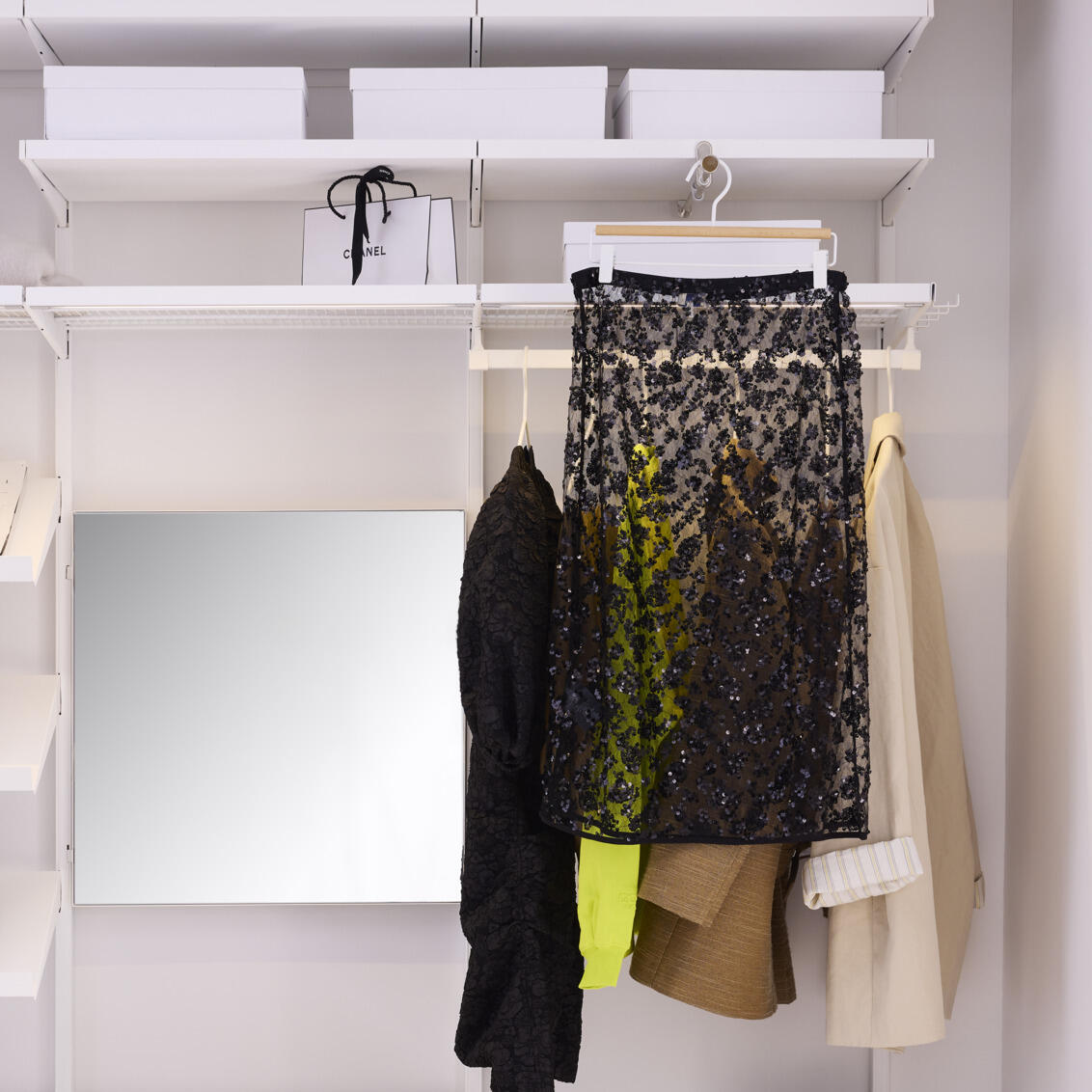 En åpen Décor+ garderobe fra Elfa med speil og uttrekkbar garderobestang med hengende svart skjørt.