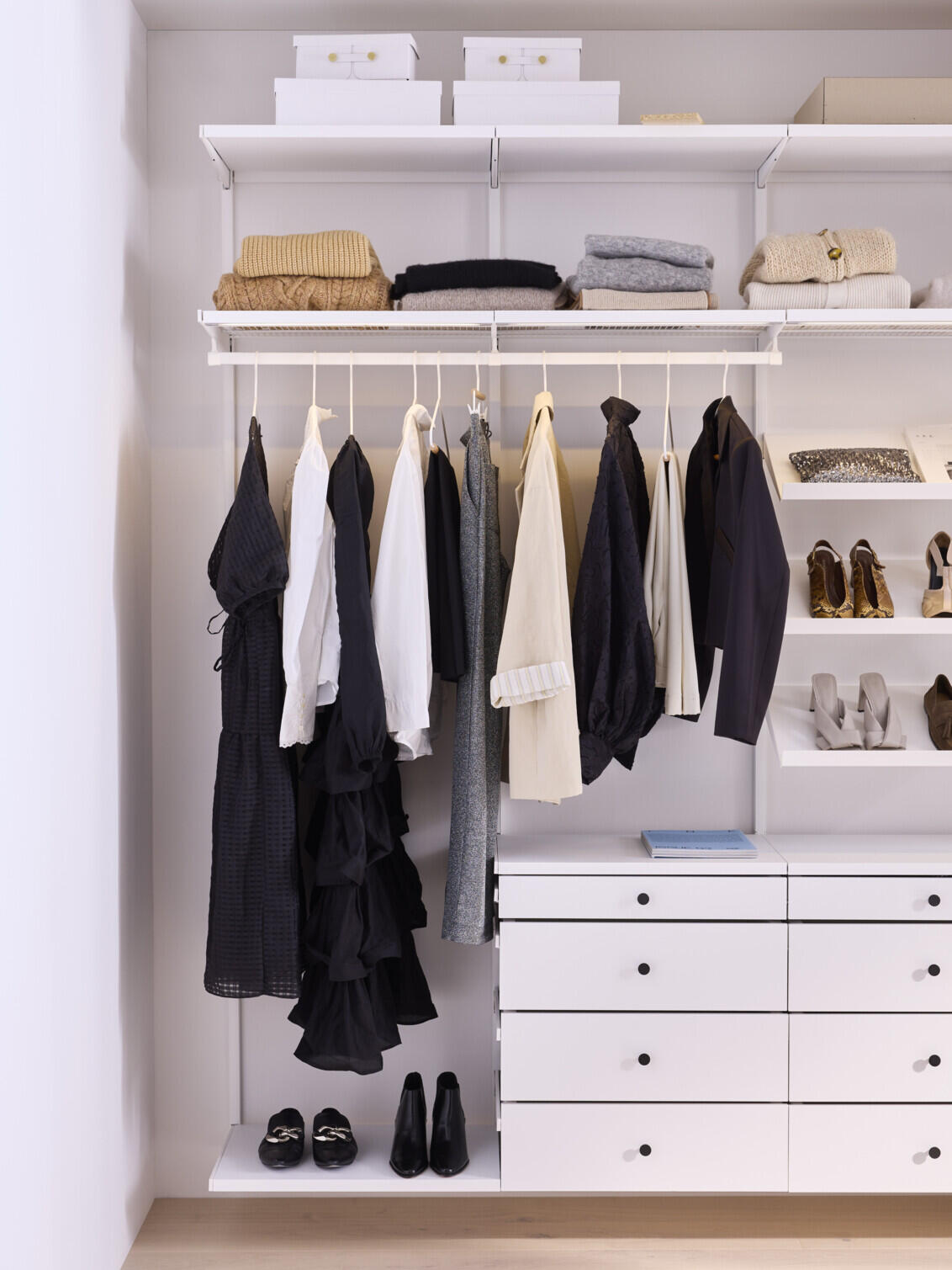 Décor+ Kleiderschrank von Elfa mit hängender Kleidung, Gitterböden, geneigten Regalböden und Schubladen in Weiß.