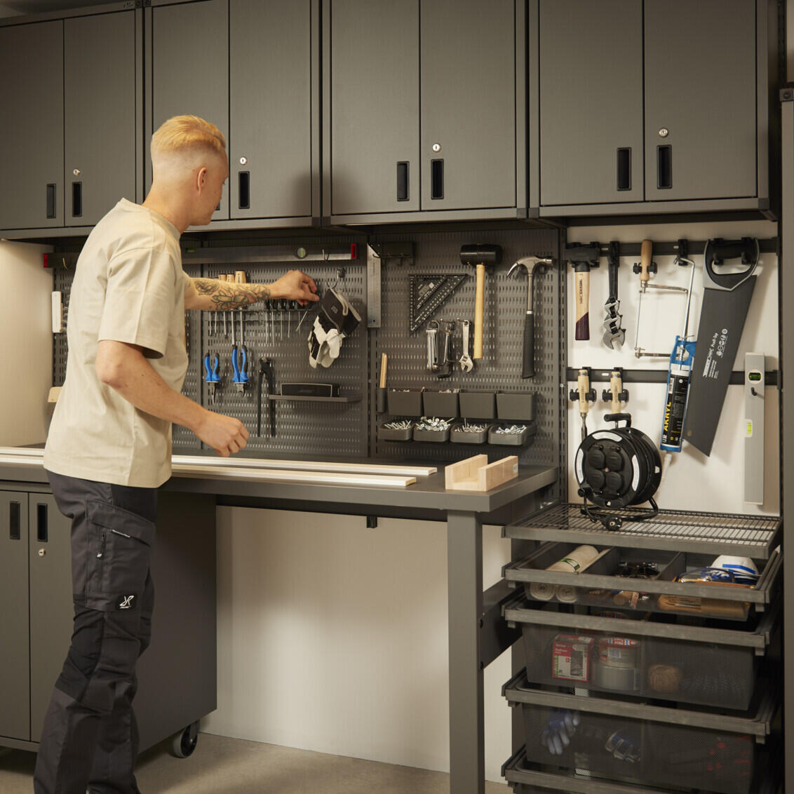 Mies tarttuu työkaluihin Elfa Garage+ -varastossa, jossa on kaappeja, säilytyslevyjä ja työpöytä.