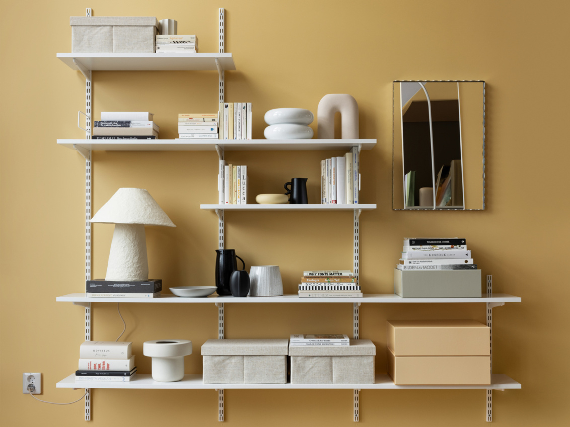 Sparring bokhylle fra Elfa i hvitt med bøker, oppbevaringsbokser og pyntegjenstander.