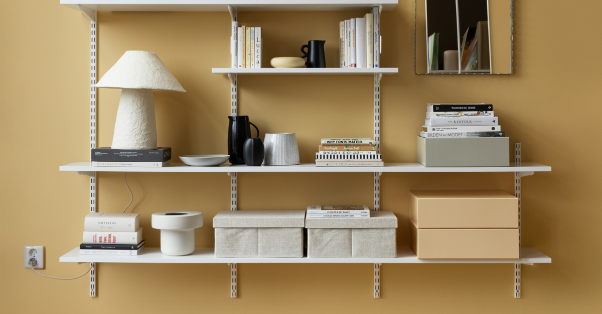 Regał Sparring Elfa w kolorze białym, z książkami, pudełkami do przechowywania i ozdobami.