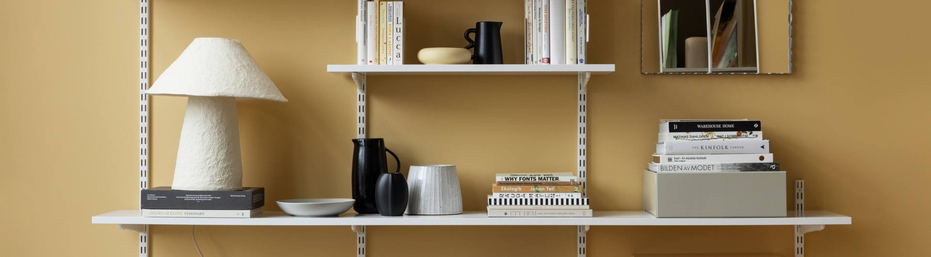 Regał Sparring Elfa w kolorze białym, z książkami, wazonami i innymi ozdobami.