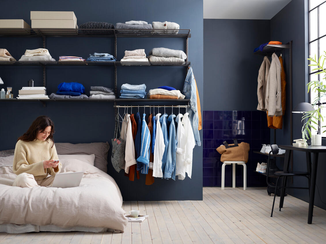 Ein Mädchen sitzt auf dem Bett in einem Schlafzimmer mit offenem Kleiderschrank in Grau von Elfa