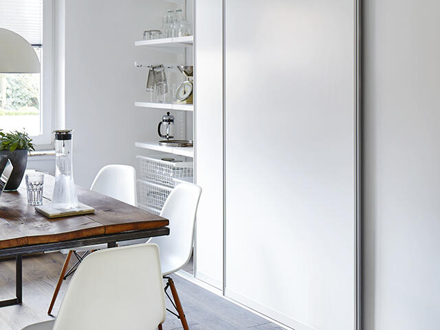 Oppbevaring av tallerkener, glass og bestikk på hyller på kjøkkenet bak arktiske skyvedører.