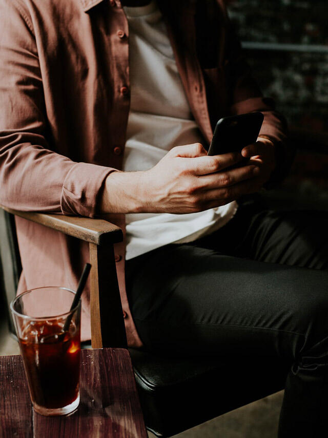 A man sits on a chair and looks at his phone.