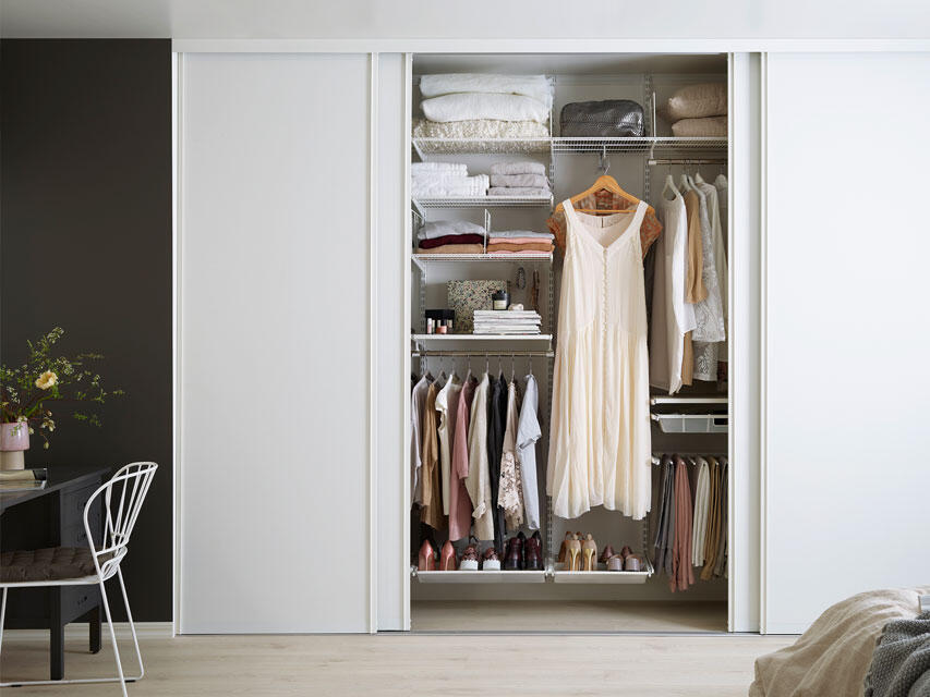 Valkoinen vaatekaappi liukuovilla ja valkoinen sisustus lankahyllyillä ja kenkätelineillä.