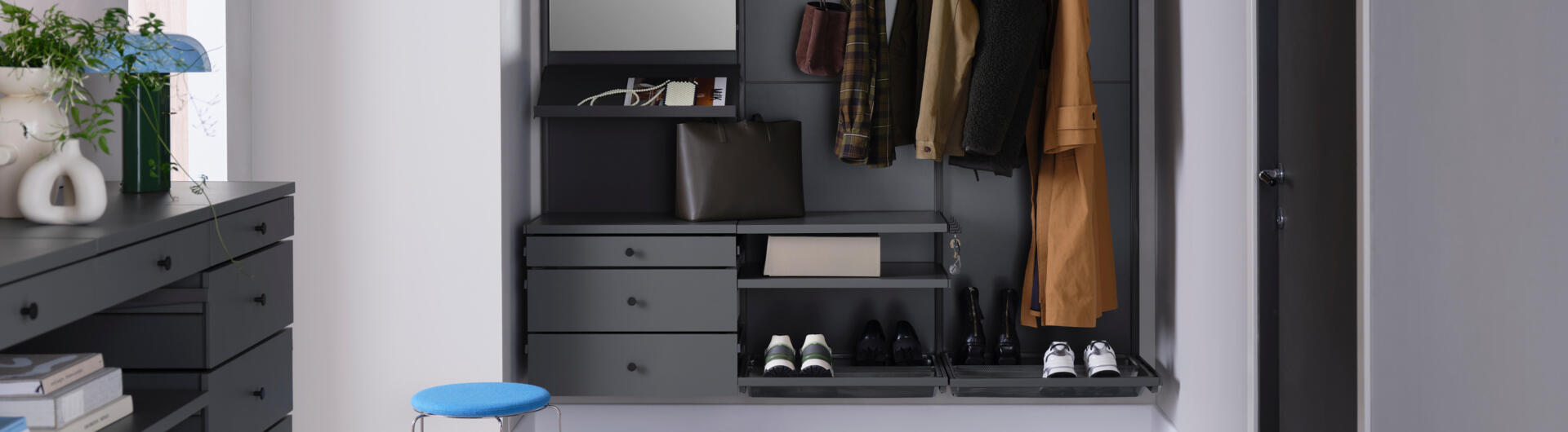 Předsíň se šatní skříní Décor+ značky Elfa v šedé barvě s výsuvnými zásuvkami, zrcadlem a koši na boty.