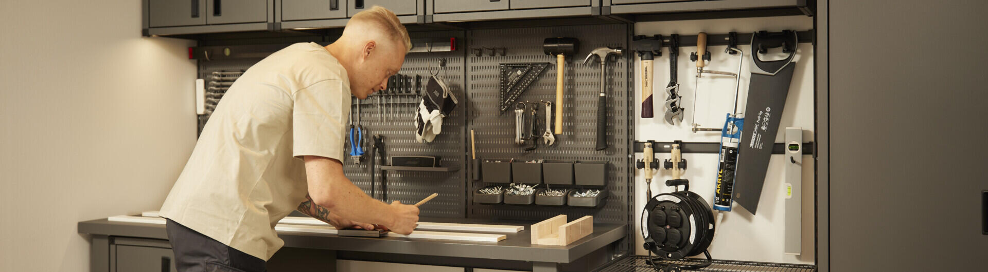 Mies seisoo autotallinsa työpöydällä, joka on sisustettu Garage+-sarjan tuotteilla.