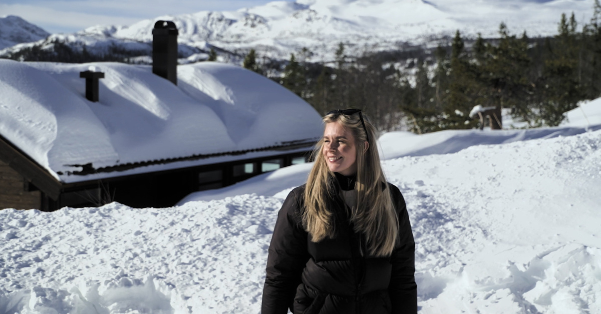 En kvinna går i snön framför en stuga.