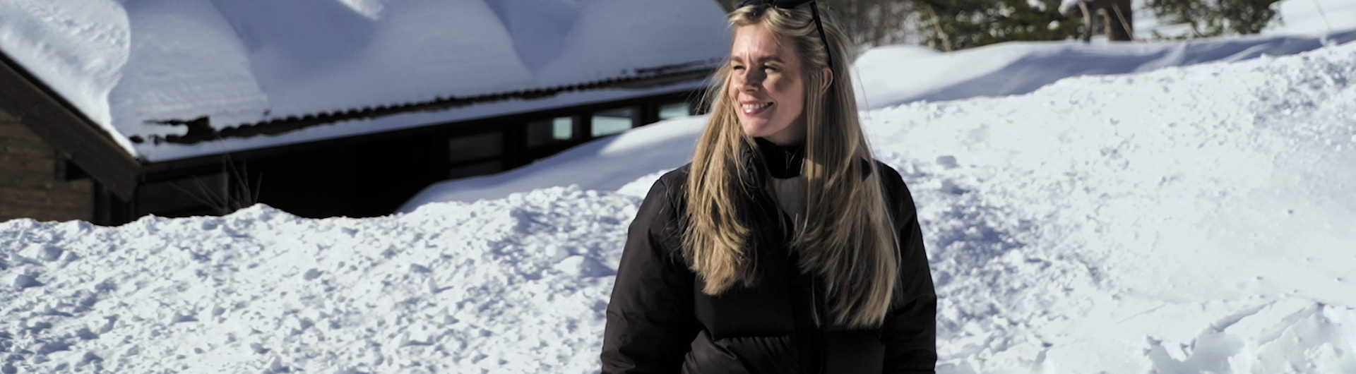 En kvinna går i snön framför en stuga.