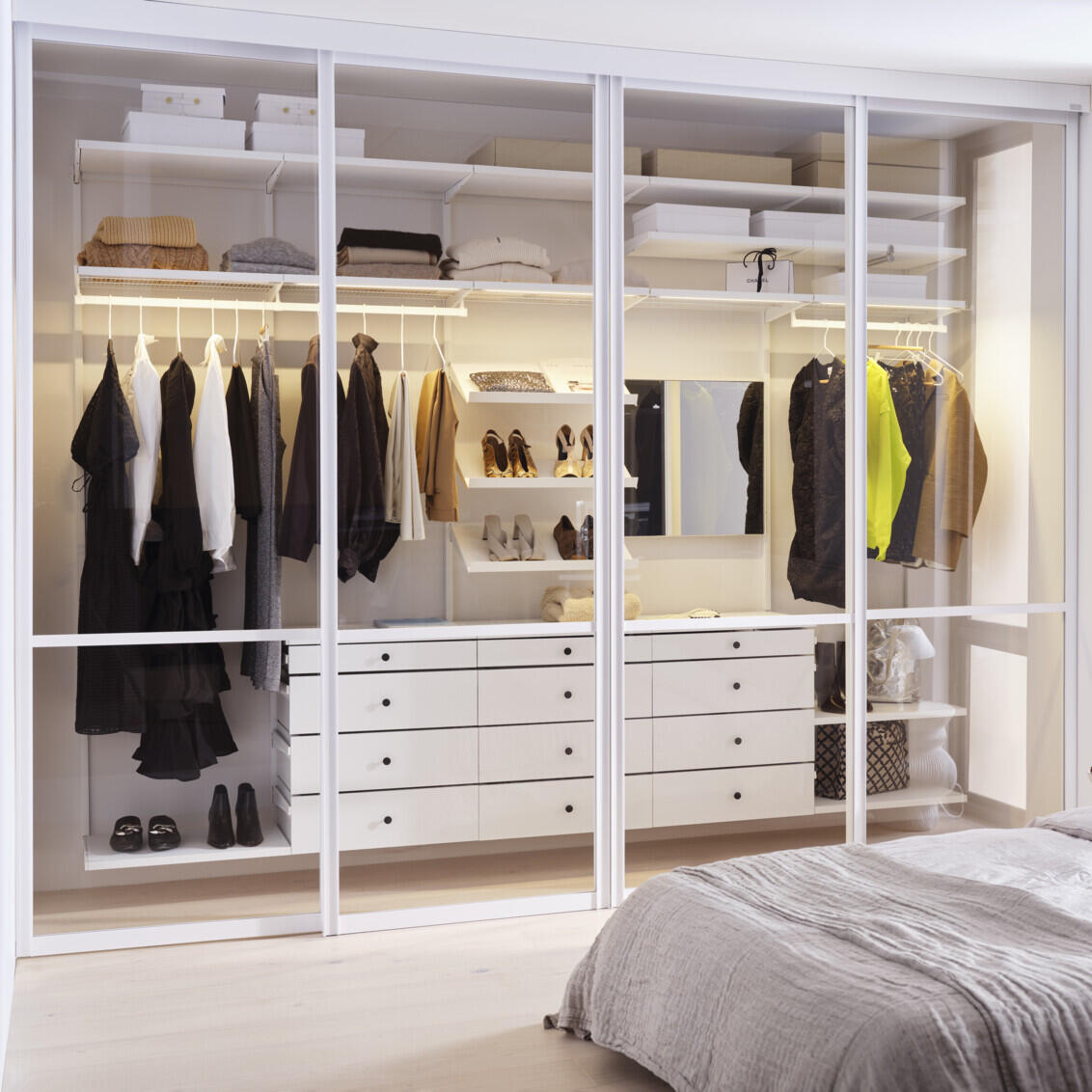 Makuuhuone, jossa on valkoinen Décor+ by Elfa -vaatekaappi, jossa on lasitäytteiset liukuovet.